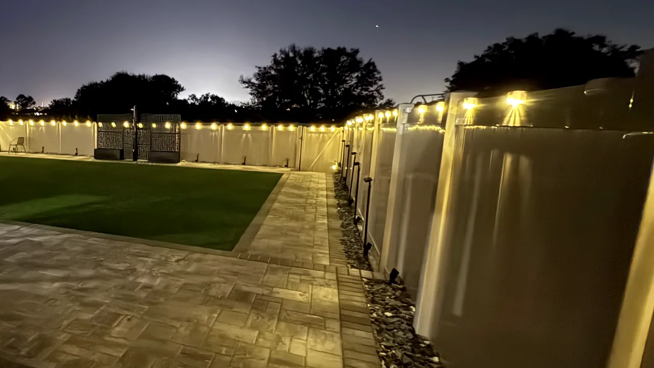 The same backyard after dark, fence lighting on and the patio in use